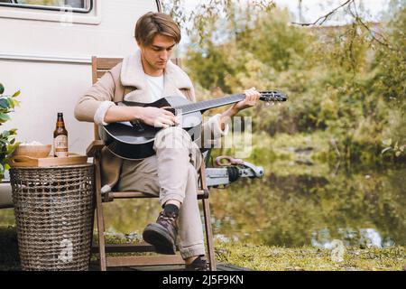 Man, guy playing guitar, traveling in camper,house on wheels,trailer,motor home.Love romantic road travel,freedom life.Campsite overnight in van.Wande Stock Photo