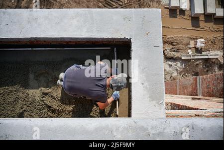 Top view of bricklayer in protective gloves working with sand and doing walls on fresh air. Concept of process building walls and modern house with good weather and modern equipments. Stock Photo