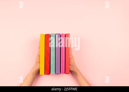 Female hands holding pile of books over pastel pink background. Education, self-learning, hobby, relax time at home Stock Photo