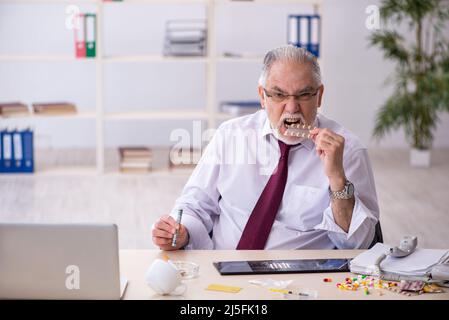 Old male drug addicted employee sitting at workplace Stock Photo