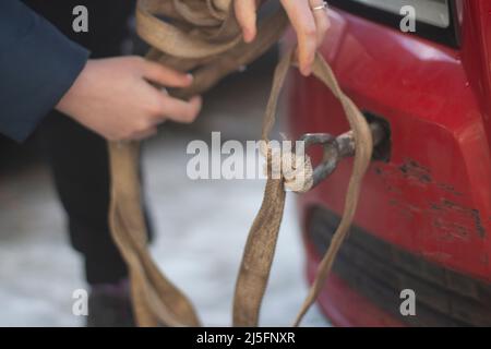 Cable for car. Guy hooks car for towing. Hand holds carabiner for screwing into bumper of car. Background preparation of vehicle evacuation. Stock Photo