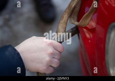 Cable for car. Guy hooks car for towing. Hand holds carabiner for screwing into bumper of car. Background preparation of vehicle evacuation. Stock Photo