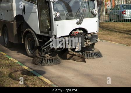 The sweeper is sweeping the asphalt. Cleaning the path with a cleaning vehicle. Cleaning the area from dust. Stock Photo