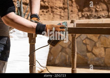 Man working on old forniture restoration using electric sander. Wood care and waterproofing concept Stock Photo