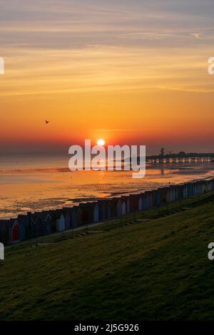 HERNE BAY: The early morning sun rising over the sea on Easter Sunday with beach huts seen in the foreground and the pier in the background. Stock Photo