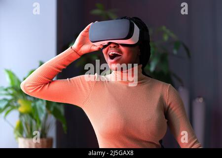Impressed black woman sitting in neon light with drop jaw wearing virtual reality headset Stock Photo