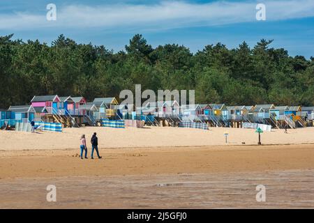 Wells Next The Sea, view on a sunny day of young people walking near colourful beach huts at Wells-next-the-Sea on the North Norfolk coast, England Stock Photo