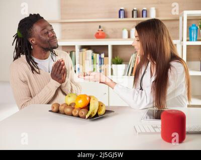 young female nutritionist in office suggests eating gingerto her patient Stock Photo