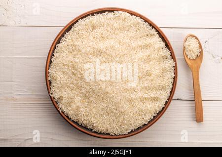 White organic raw rice in a clay plate with a wooden spoon on a wooden table, close-up, top view. Stock Photo