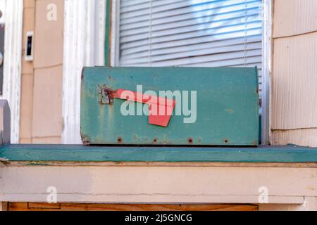 Old dark green mailbox on a green wooden surface at San Francisco, California. Rusty mailbox with down red flag against the view of light brown wall a Stock Photo