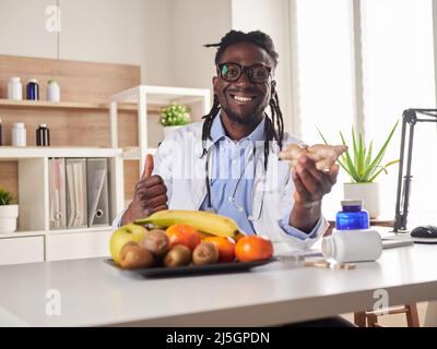 Afroamerican nutritionist looking at camera and showing healthy fruits in the consultation. Stock Photo