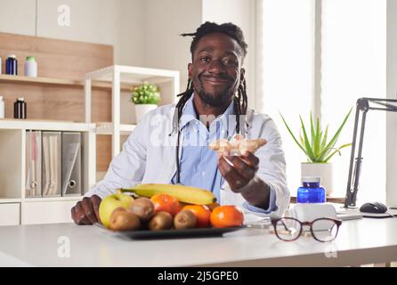 Afroamerican nutritionist looking at camera and showing healthy fruits in the consultation. Stock Photo