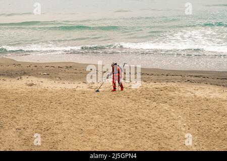 Man with a metal detector walks along the beach in a red suit. Slow motion, 4k, slow motion Stock Photo