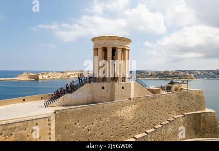 A group of tourists sitting on the steps of the Siege Bell memorial, Valletta, Malta Stock Photo