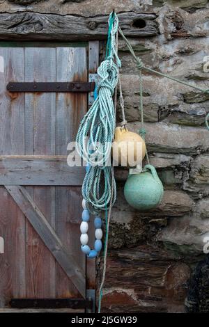 Old bouys with tidily coiled blue rope hanging on stone wall, weathered wooden door, Hope Cove, Devon Stock Photo