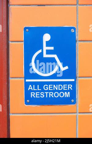 Blue sign with all gender restroom note and PWD symbol at San Francisco, California. Close-up of a nailed signage on a wall with orange tiles at the b Stock Photo