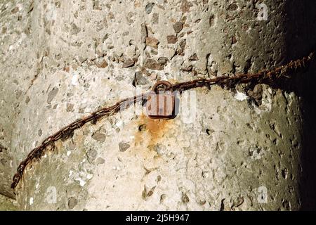 an old rusty padlock closed on a rusty chain against a concrete wall. Stock Photo