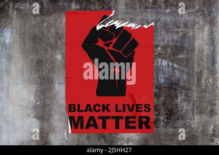 Full-frame weathered concrete wall with a torn red poster in the middle dispicting a black fist with "Black lives matter" written bellow. Stock Photo