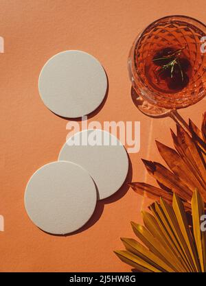 Boho style blank paper trivet drip mat coasters with a wine cocktail glass and dried palm leaves next to them, to be used as a Mockup Stock Photo