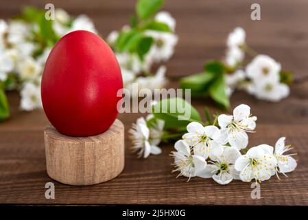 A red decorated Easter egg on a pedestal and blooming spring flowers on a rustic wooden table. Easter concept. Stock Photo