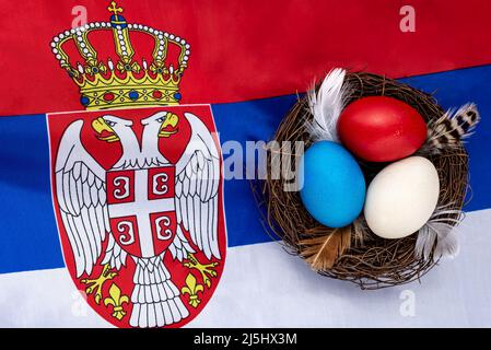 Multicolored decorated Easter eggs in a nest on the flag of Serbia. Easter concept. Stock Photo