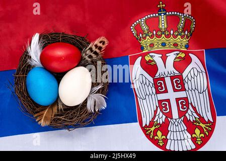 Multicolored decorated Easter eggs in a nest on the flag of Serbia. Easter concept. Stock Photo