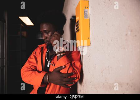 Black prisoner in an orange jumpsuit talking to the phone. Stock Photo