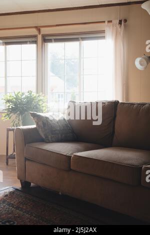 Moody living room with couch by window. Sunlight shines on sofa.  Stock Photo