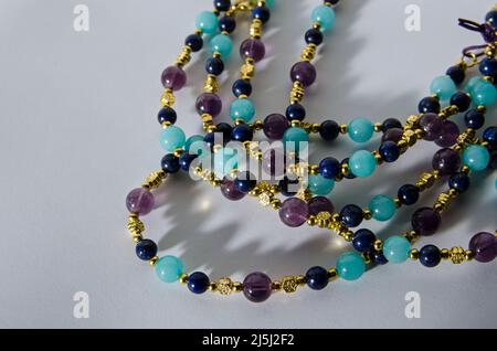 Coils of a necklace handmade from beads of purple amethyst, blue lapis lazuli and turquoise quartzite gemstones.  Viewed on a white background with dr Stock Photo