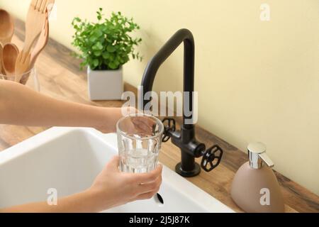 Woman pouring water from faucet into glass near color wall, closeup Stock Photo