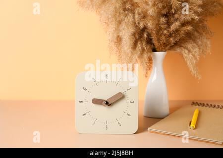 Alarm clock, notebook and vase with pampas grass on table near color wall Stock Photo