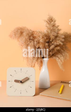 Alarm clock, notebook and vase with pampas grass on table near color wall Stock Photo