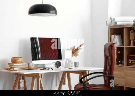 Modern computer, different gadgets, alarm clock and books on table near light wall Stock Photo