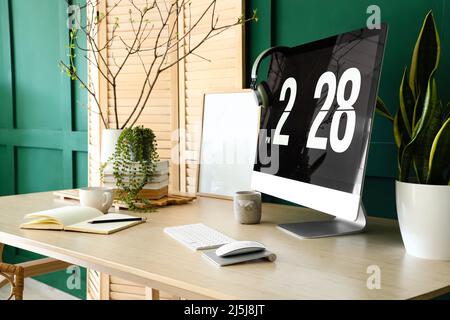 Modern computer and houseplants on table near green wall Stock Photo