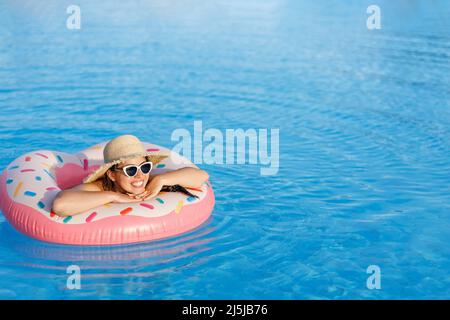 young woman in straw hat and sunglasses relaxing on inflatable ring in swimming pool Stock Photo