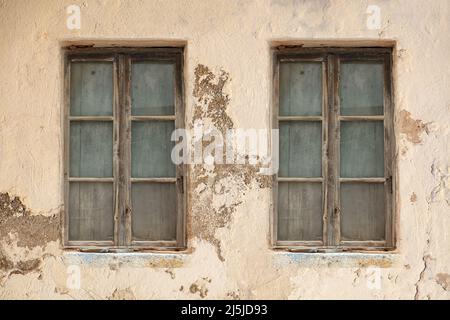 Derelict home concept. Two windows covered with inside wooden planks, weathered aged on peeled wall background. Abandoned shabby worn building exterio Stock Photo