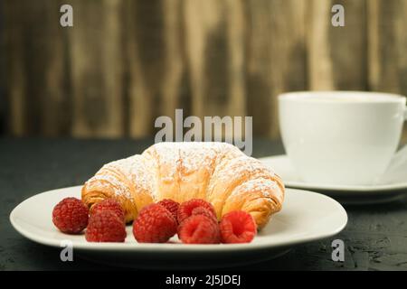 Croissants and fresh raspberries, Fresh and delicious croissants. Breakfast at the hotel: coffee with milk and croissants, fresh raspberries on a wood Stock Photo