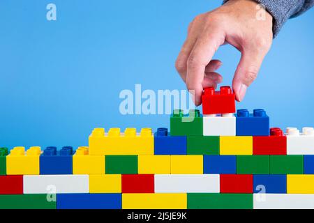 hand building up a wall by stacking up plastic block on blue background Stock Photo