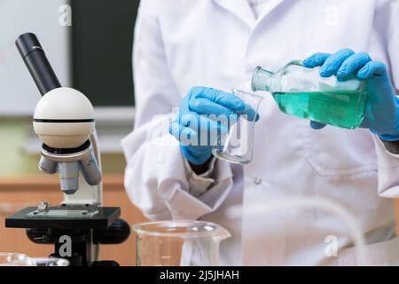 Scientist pouring substance from one flask to another in a laboratory during research work Stock Photo