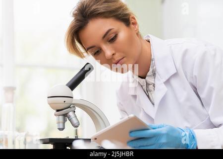 Woman scientist is using microscope and tablet pc in a laboratory during research work Stock Photo