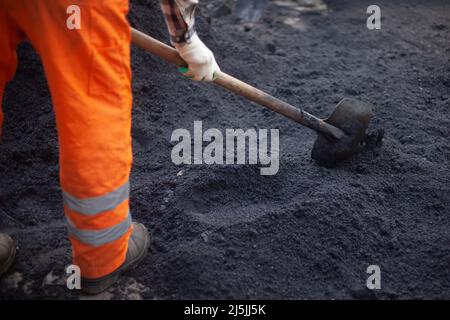 A bunch of asphalt. Workers repair the road. People in orange clothes. Asphalt pavement. Men work with shovels. Stock Photo