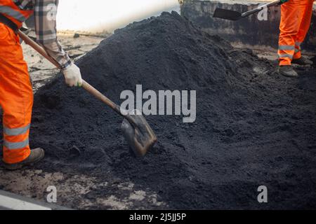 A bunch of asphalt. Workers repair the road. People in orange clothes. Asphalt pavement. Men work with shovels. Stock Photo