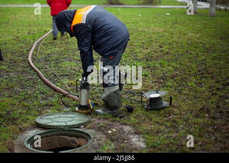 Repair of heating pipes. Workers near the manhole. Equipment for measuring pressure in pipes. Lowering the pump underground. Stock Photo