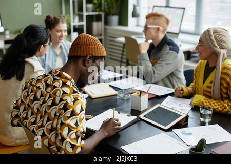 Back view at young black man taking notes in meeting with creative business team in office Stock Photo