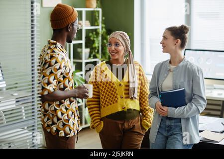 Waist up portrait of three creative young people chatting during coffee break in office Stock Photo