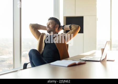Contented Businessman Relaxing Holding Hands Behind Head Sitting In Office Stock Photo