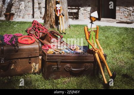 Pinocchio puppet sitting on a leather suitcase. Beautiful flea market on a garden. Stock Photo