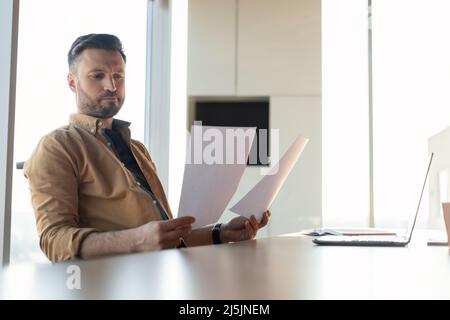 Thoughtful Businessman Reading Business Papers Holding Documents Sitting In Office Stock Photo
