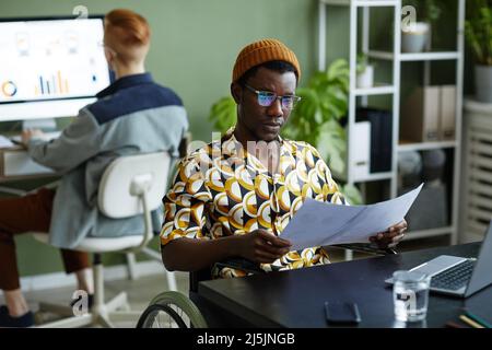Portrait of black young man reading documents and wearing creative style while working in office Stock Photo