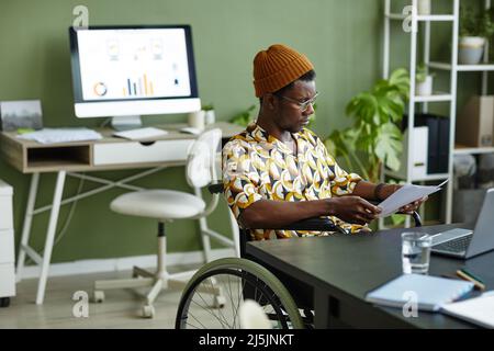 Portrait of black young man in wheelchair wearing creative style while working in office, copy space Stock Photo